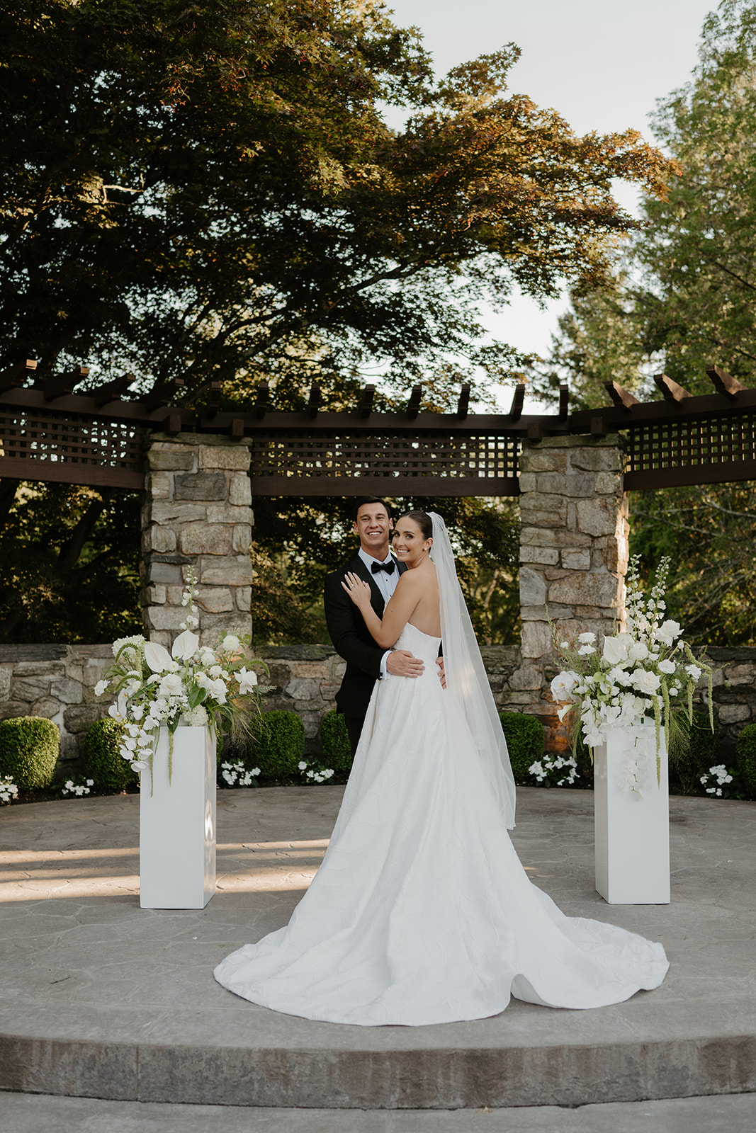 Bride looking over her shoulder with a warm smile while embracing the groom at the stone altar.